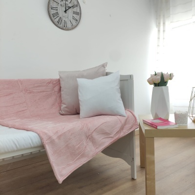 Sofá-cama branco com colcha rosa e almofadas, mesa dourada com vaso e livro em ambiente claro