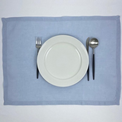 Individual de mesa azul claro com prato branco e talheres preto