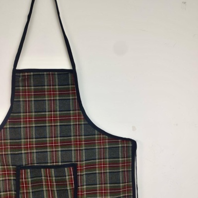 Avental xadrez com bordas pretas pendurado numa parede branca