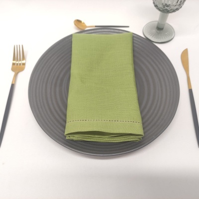 Conjunto de jantar com prato cinzento, guardanapo verde, talheres dourados e copo de vidro.