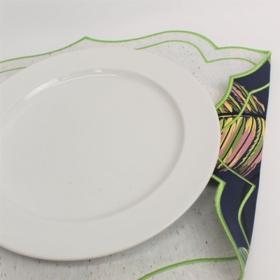 Prato branco em pano de mesa branco com bordas verdes e padrão colorido