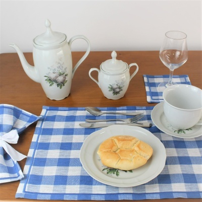 Conjunto de chávenas e bule com padrão floral sobre toalha azul e branca xadrez