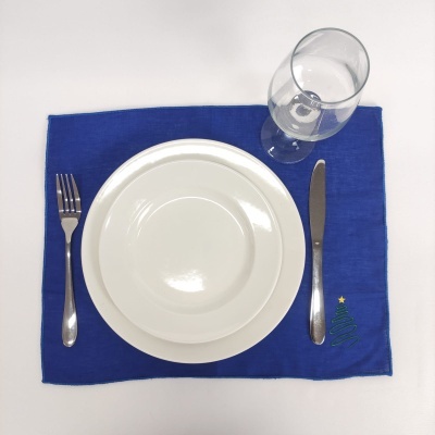 Conjunto de mesa com jogo americano azul com padrão de árvore de Natal, talheres, pratos brancos e copo de vidro