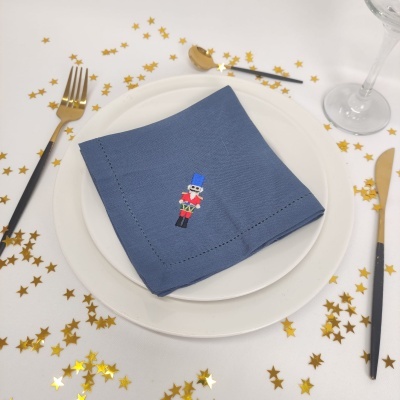 Guardanapo azul bordado com soldado quebra-nozes em prato branco, decoração com confetes dourados e talheres dourados e pretos