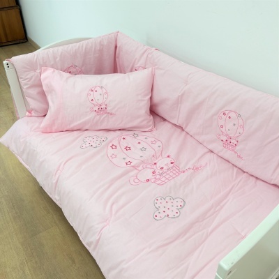 Roupa de cama infantil cor-de-rosa com desenhos bordados de balões, nuvens e ursos numa cama branca