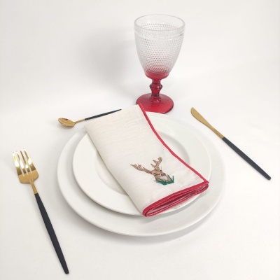 Conjunto de louça branca com guardanapo bordado, talheres preto e dourado e copo vermelho