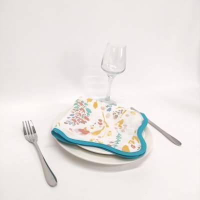 Mesa posta com prato branco, guardanapo floral colorido, talheres metálicos e copo de vidro