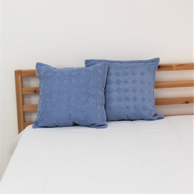 Duas almofadas azuis com textura apoiadas numa cama com cabeceira de madeira.