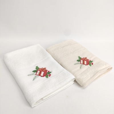 Duas toalhas dobradas branca e bege claro com bordado de presente vermelho e folhas verdes