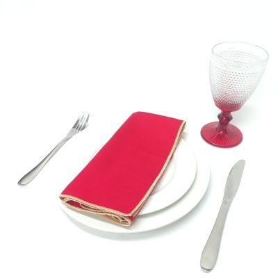 Conjunto de mesa com prato branco, talheres metálicos, guardanapo vermelho e copo de vidro com base vermelha