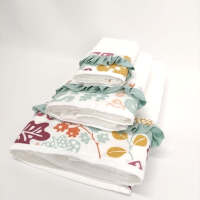 Conjunto de toalhas brancas com bordados florais e folhos verdes empilhadas