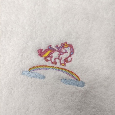 Toalha branca com bordado de unicórnio colorido sobre arco-íris e nuvens