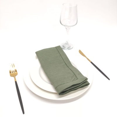 Conjunto de mesa com pratos brancos, guardanapo verde, talheres com cabo preto e dourado e taça de vidro.