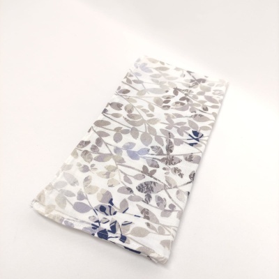 Toalha branca com estampa floral cinzenta, azul e bege dobrada sobre fundo branco