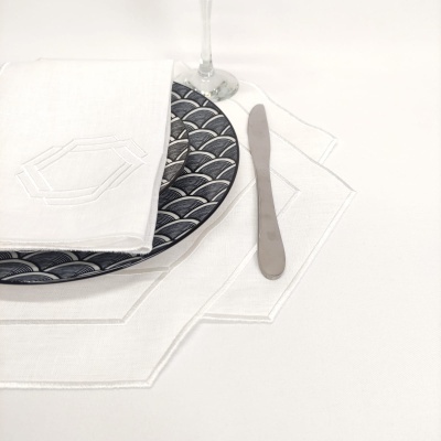 Conjunto de loiça azul escuro com padrão de escamas, guardanapo, pega de mesa em linho branco com bordado, faca e copo de vidro.