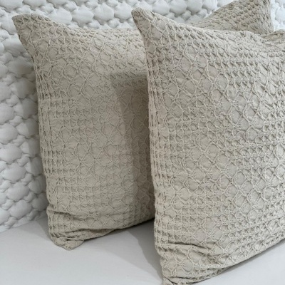 Duas almofadas bege com padrão de rede texturizada sobre superfície clara e fundo branco acolchoado