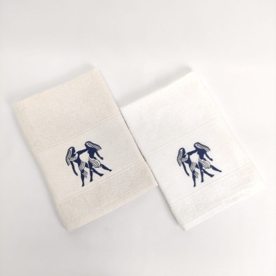 Duas toalhas de banho com bordado azul de figura feminina com chapéu, uma bege e outra branca