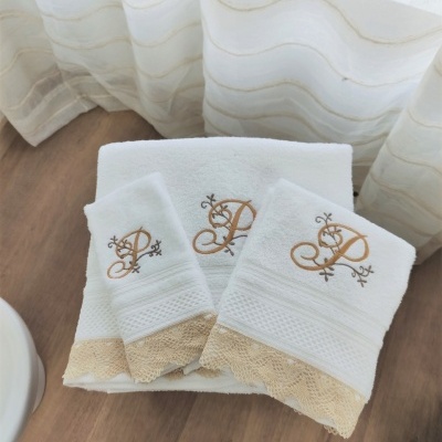 Toalhas brancas de algodão com bordado dourado e renda bege numa superfície de madeira