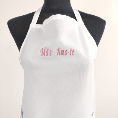 Avental branco bordado com texto cor-de-rosa à frente, exposto em manequim preto.
