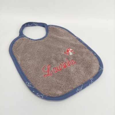 Babete para bebé castanho com bordas azuis e bordado com o nome Laurinha e desenho de barco