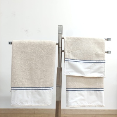 Conjunto de toalhas bege com faixa branca e linha azul penduradas em suporte metálico