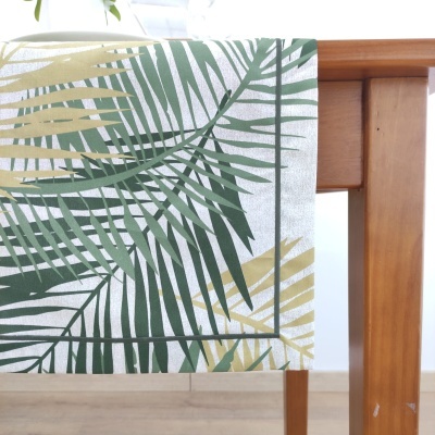 Toalha de mesa decorativa com padrão de folhas verdes e amarelas pendurada em mesa de madeira.