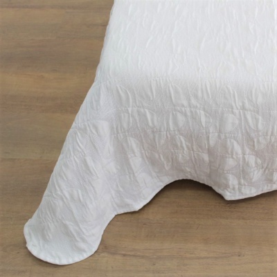 Colcha branca com textura em relevo sobre chão de madeira clara