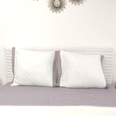 Cama com lençol lilás e almofadas brancas com borda lilás