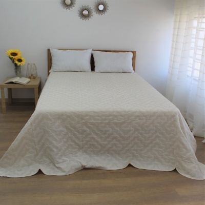 Cama com colcha branca texturizada e almofadas, mesa de cabeceira com girassóis e livro, quarto branco com cortina translúcida