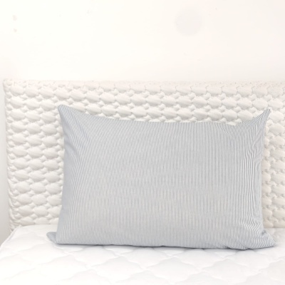 Travesseiro com capa listrada cinza e branco sobre colchão e cabeceira brancos acolchoados