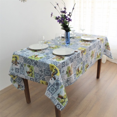 Toalha de mesa com padrão de azulejos azuis e amarelos, mesa posta com pratos, copos e vaso com flores