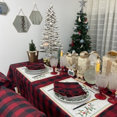 Mesa de Natal com toalha xadrez vermelha e preta, decoração natalícia e copos com base vermelha.