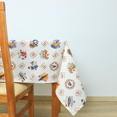 Toalha de mesa branca com padrões coloridos de motivos náuticos e florais sobre mesa de madeira