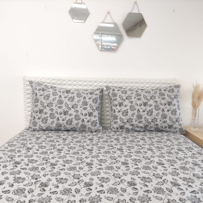 Roupa de cama branca com padrão floral preto sobre cama com cabeceira branca e espelhos hexagonais na parede