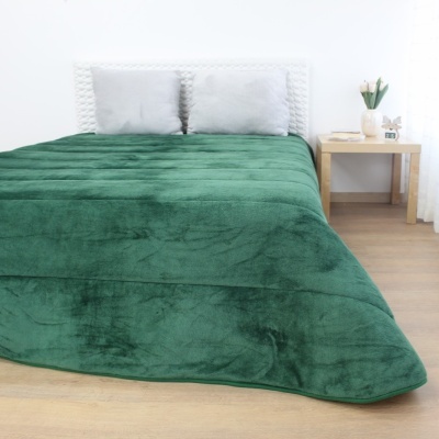 Cama com manta verde e mesa de cabeceira com vaso branco e flores