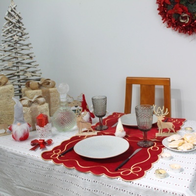 Mesa de jantar de Natal com decoração vermelha, branca e dourada, figuras de renas, velas e toalha bordada