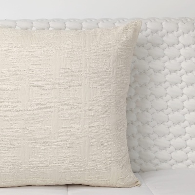 Almofada bege claro com tecido texturado sobre capa de sofá branca acolchoada