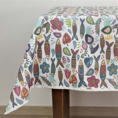 Toalha de mesa branca com padrão colorido de peixes e flores sobre mesa de pernas de madeira.