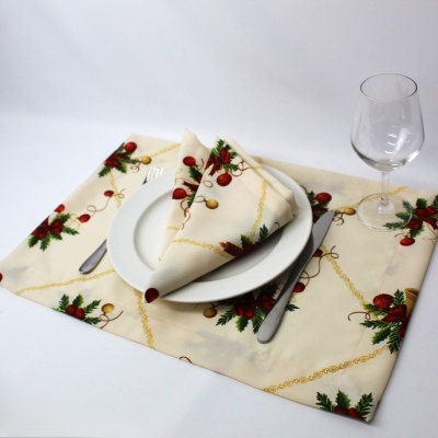 Jogo americano e guardanapo natalício com bolas vermelhas e douradas e folhas verdes, prato branco, talheres e copo de vidro.