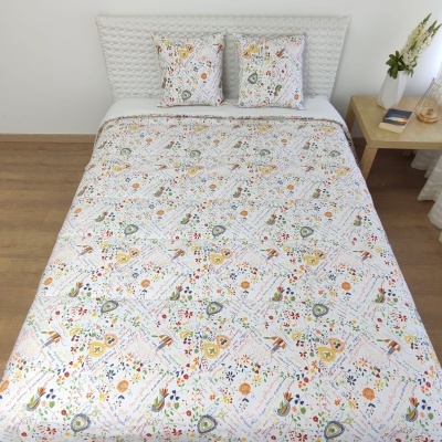 Colcha e almofadas com padrão floral colorido numa cama com cabeceira branca, ao lado uma mesa de apoio com jarra e livro.