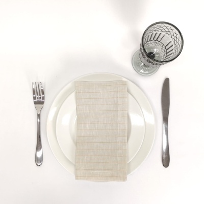 Conjunto de mesa com prato branco, guardanapo bege, talheres de inox e copo de vidro decorado