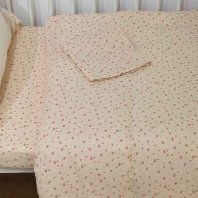 Roupas de cama bege com flores cor-de-rosa num berço branco.