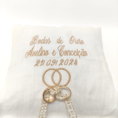 Toalha branca com bordado dourado, anéis entrelaçados e alianças metálicas
