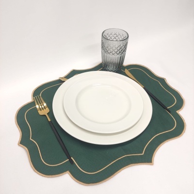 Conjunto de pratos brancos sobre jogo americano verde com garfo dourado, faca preta e copo transparente