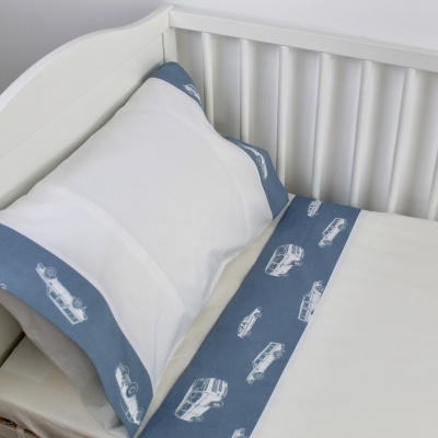 Jogo de cama branco com bordas azuis e padrões de veículos em berço branco