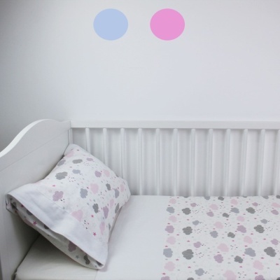 Berço branco com lençol e almofada estampados com nuvens e bolas coloridas na parede