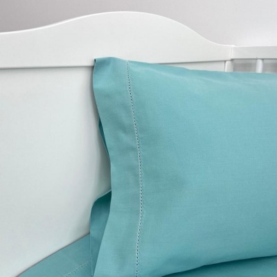Almofada e lençol azul celeste com costuras decorativas numa cama com cabeceira branca
