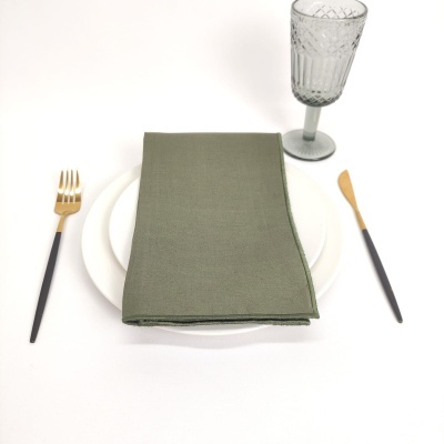 Conjunto de mesa com prato branco, guardanapo verde, talheres com cabo preto e dourado e copo de vidro cinza