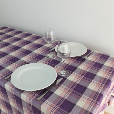 Mesa com toalha xadrez roxa, pratos brancos, copos de vinho e talheres