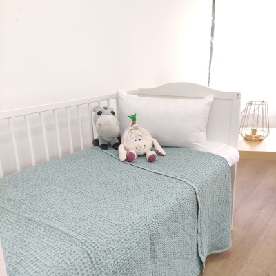 Cama infantil branca com manta verde e peluches